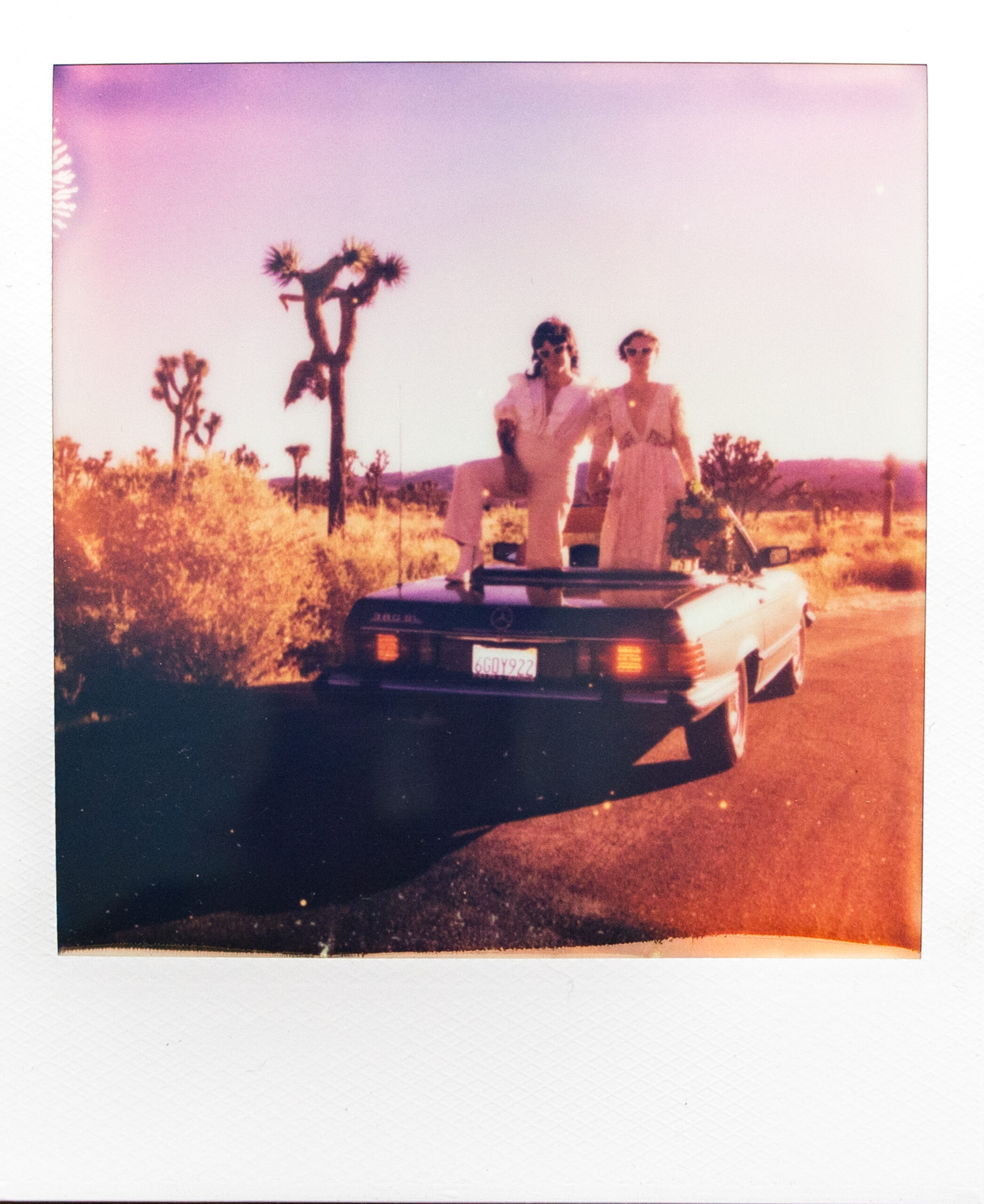 Polaroid of two brides standing in convertible vintage car in Joshua Tree