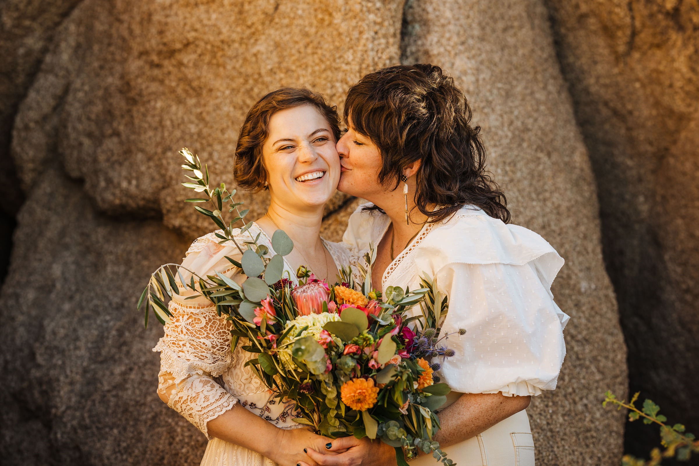 Two brides eloping in Joshua Tree kiss on cheek